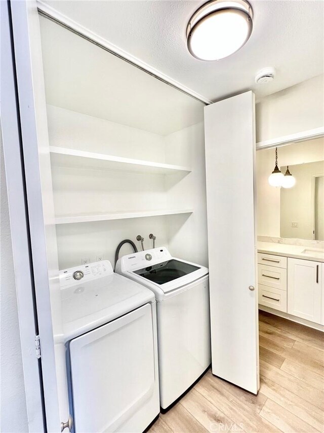 laundry room with sink, washing machine and dryer, light hardwood / wood-style floors, and a textured ceiling