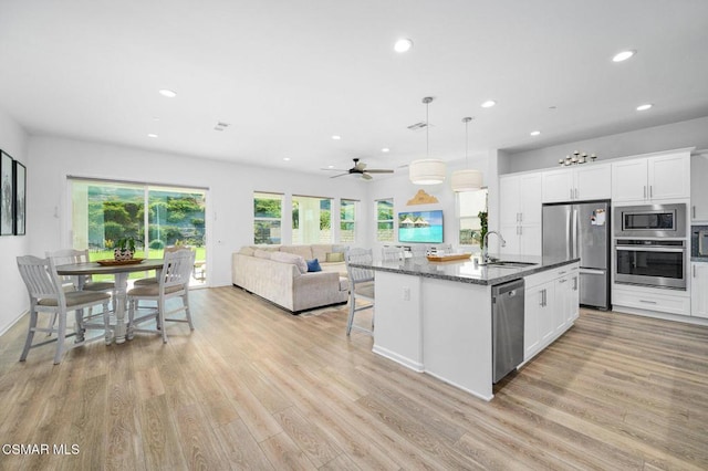 kitchen with appliances with stainless steel finishes, dark stone countertops, white cabinetry, a center island with sink, and decorative light fixtures