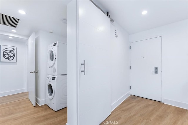 washroom with stacked washer / dryer, a barn door, and light wood-type flooring