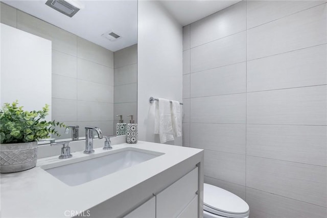 bathroom with tile walls, vanity, and toilet