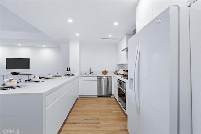 kitchen with sink, light hardwood / wood-style flooring, appliances with stainless steel finishes, white cabinets, and kitchen peninsula