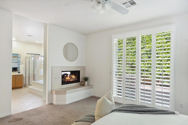 carpeted bedroom with a tiled fireplace, connected bathroom, and ceiling fan