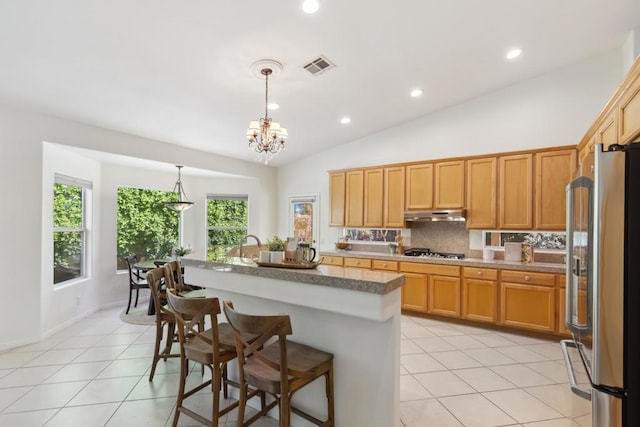 kitchen featuring high end fridge, gas stovetop, light tile patterned floors, pendant lighting, and a kitchen island with sink