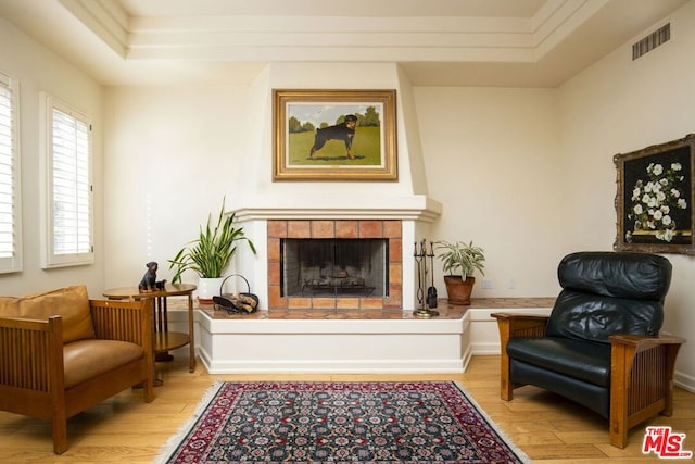 living area featuring light hardwood / wood-style flooring, a tile fireplace, and a raised ceiling