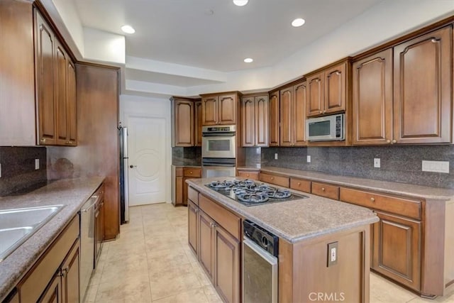 kitchen featuring appliances with stainless steel finishes, sink, light tile patterned floors, a kitchen island, and tasteful backsplash