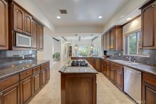 kitchen featuring decorative light fixtures, a kitchen island, sink, backsplash, and appliances with stainless steel finishes