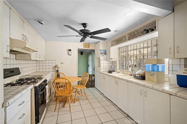 kitchen with sink, tile countertops, gas stove, and white cabinets