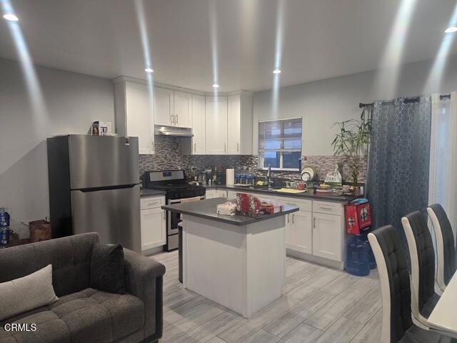 kitchen with sink, white cabinetry, stainless steel appliances, a kitchen island, and decorative backsplash