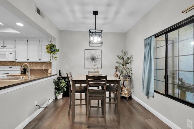 dining area with dark wood-type flooring, sink, and a notable chandelier