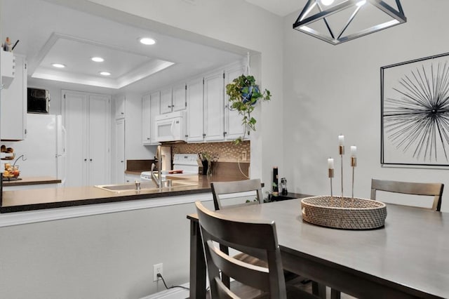 kitchen with tasteful backsplash, a tray ceiling, kitchen peninsula, white appliances, and white cabinets