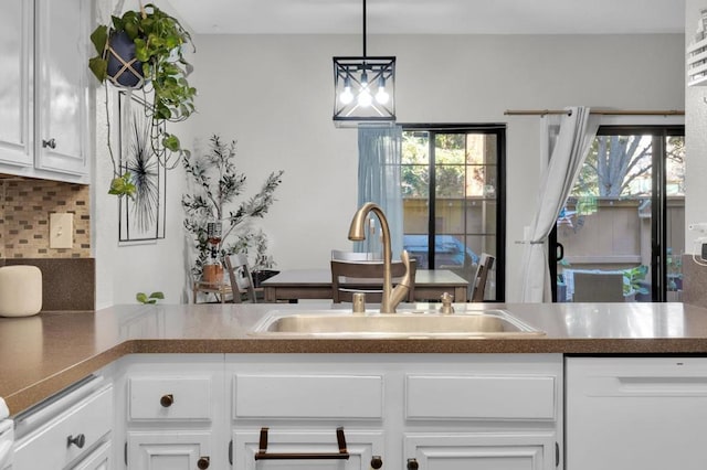 kitchen featuring sink, backsplash, white dishwasher, white cabinets, and decorative light fixtures