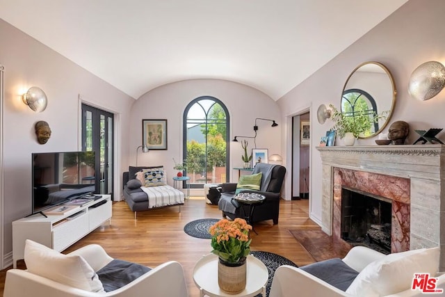 living room featuring a high end fireplace, vaulted ceiling, and light hardwood / wood-style floors