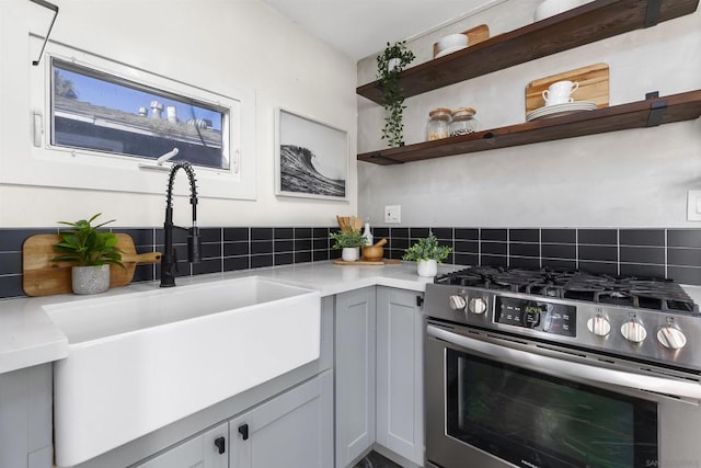 kitchen featuring gray cabinets, stainless steel gas range oven, sink, and tasteful backsplash