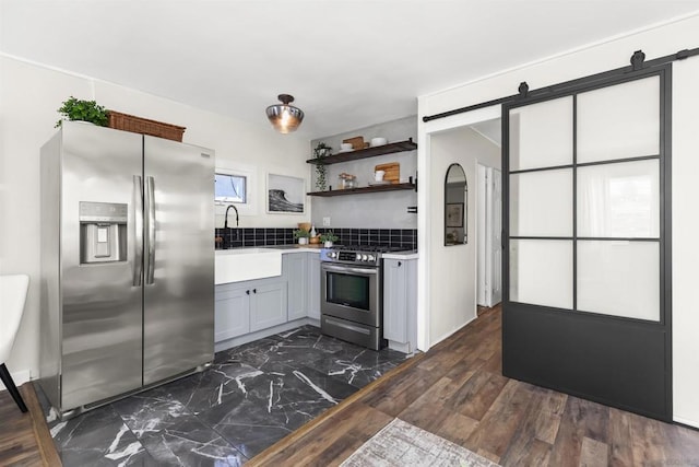 kitchen featuring sink, decorative backsplash, stainless steel appliances, a barn door, and dark wood-type flooring