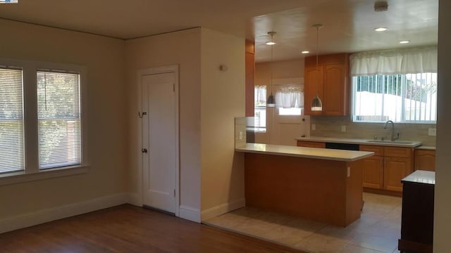 kitchen featuring decorative light fixtures, sink, decorative backsplash, light hardwood / wood-style floors, and kitchen peninsula