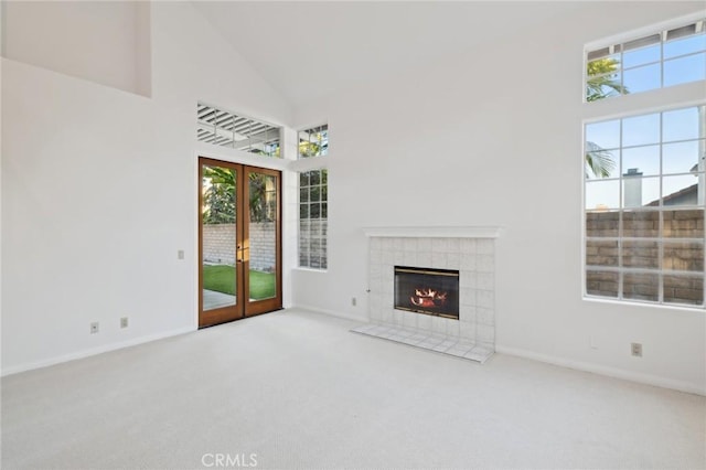 unfurnished living room featuring a tiled fireplace, carpet floors, high vaulted ceiling, and french doors