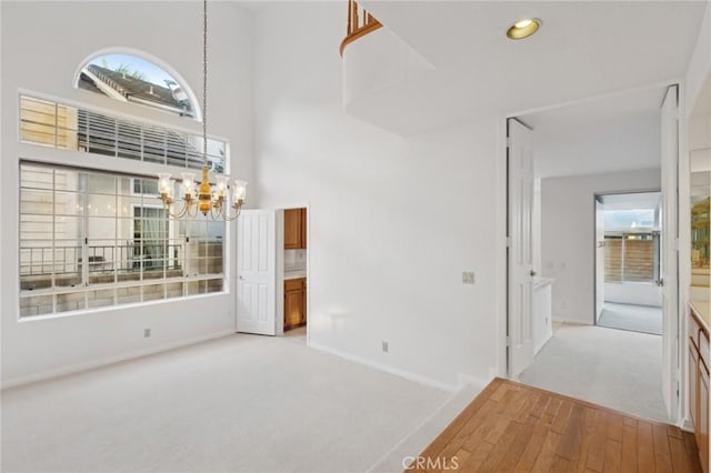 carpeted spare room featuring a high ceiling, a wealth of natural light, and a chandelier