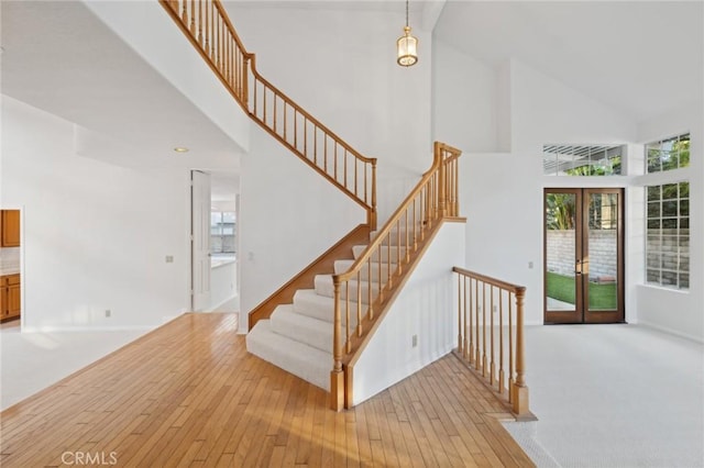 staircase featuring french doors, high vaulted ceiling, and hardwood / wood-style flooring