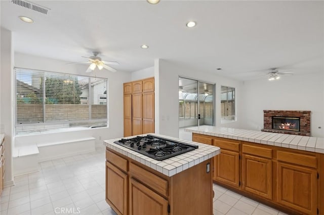 kitchen with ceiling fan, black gas cooktop, a fireplace, a kitchen island, and tile countertops