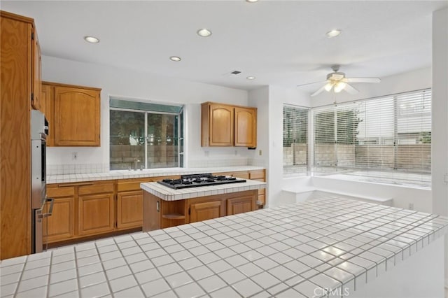 kitchen with ceiling fan, tile countertops, a center island, and stainless steel gas stovetop