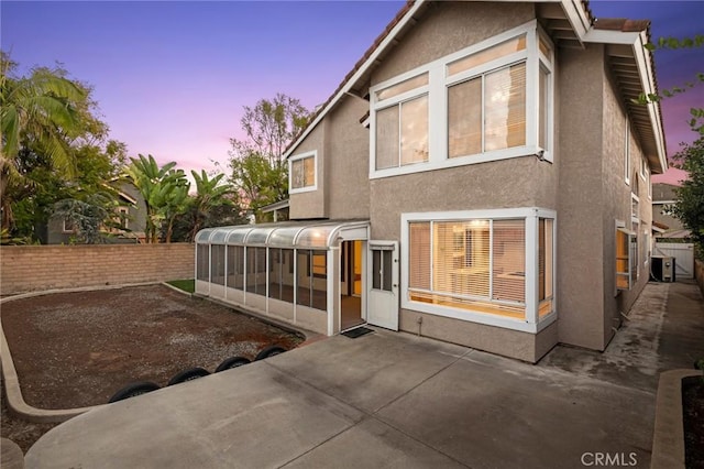 back house at dusk with a patio and a sunroom