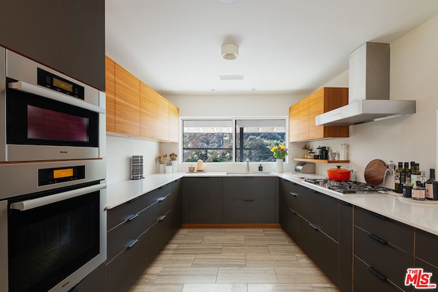 kitchen featuring appliances with stainless steel finishes, sink, and wall chimney range hood