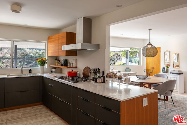 kitchen with sink, hanging light fixtures, stainless steel gas cooktop, wall chimney exhaust hood, and light hardwood / wood-style flooring