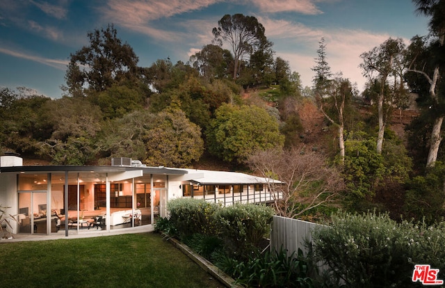 back house at dusk featuring a yard and a patio