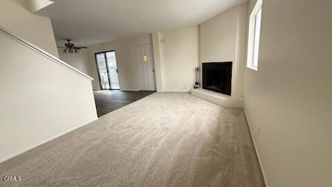 unfurnished living room with ceiling fan, stairway, baseboards, a fireplace with raised hearth, and carpet