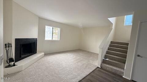 unfurnished living room with a fireplace with raised hearth, stairs, and wood finished floors