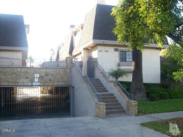 view of side of property featuring a chimney, a gate, stairway, a shingled roof, and stucco siding