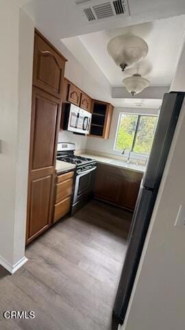 kitchen with a tray ceiling, visible vents, brown cabinets, light wood-style floors, and stainless steel appliances