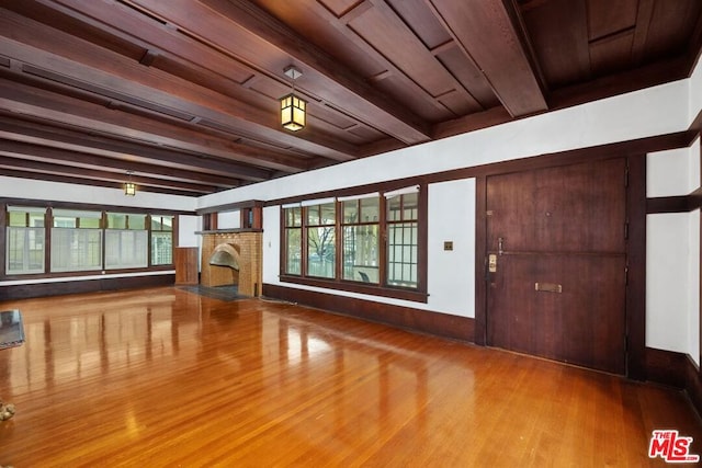 foyer entrance with a brick fireplace, beam ceiling, a healthy amount of sunlight, and hardwood / wood-style flooring