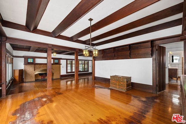 unfurnished living room with beam ceiling, a brick fireplace, and hardwood / wood-style flooring