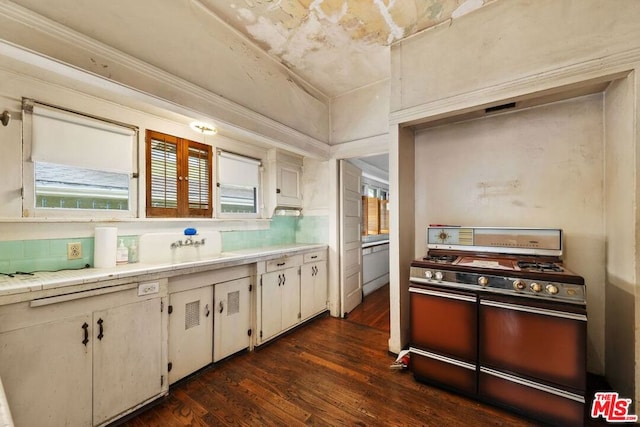 kitchen with sink, backsplash, white cabinets, dark hardwood / wood-style flooring, and range with two ovens