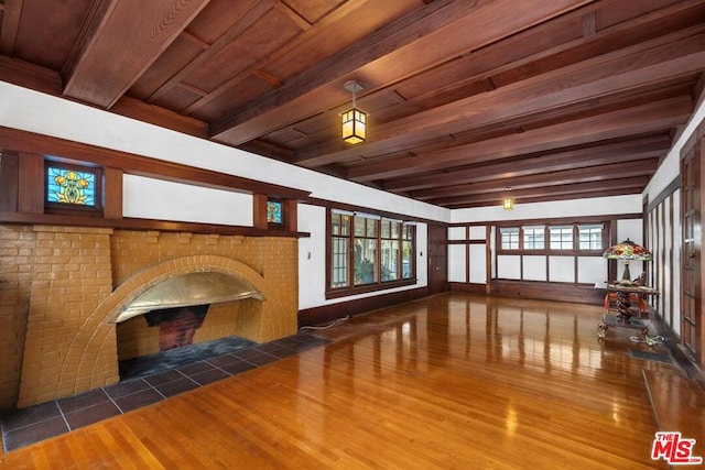 unfurnished living room with beamed ceiling, a brick fireplace, dark hardwood / wood-style floors, and a wealth of natural light