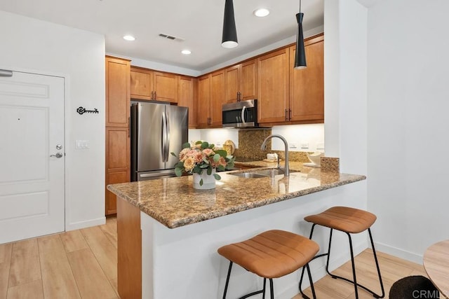 kitchen featuring stainless steel appliances, stone countertops, sink, and light hardwood / wood-style flooring