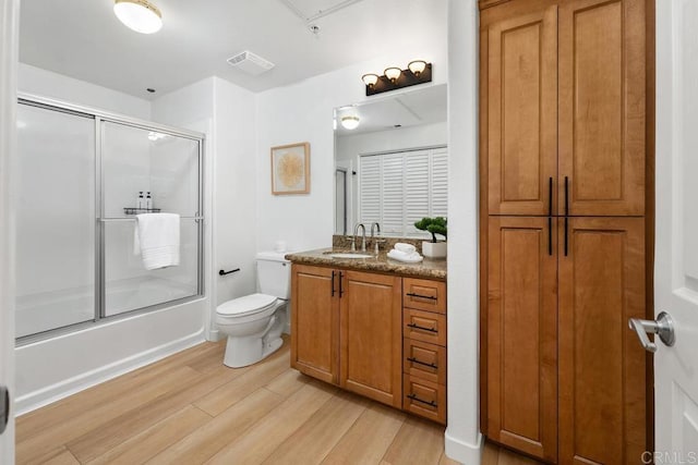 full bathroom featuring enclosed tub / shower combo, vanity, hardwood / wood-style floors, and toilet