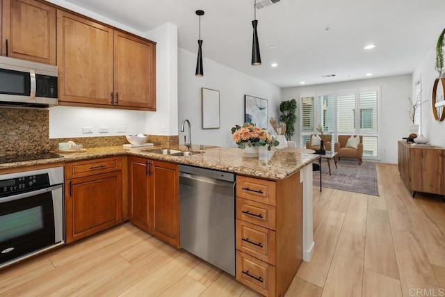 kitchen featuring sink, decorative light fixtures, appliances with stainless steel finishes, kitchen peninsula, and light stone countertops