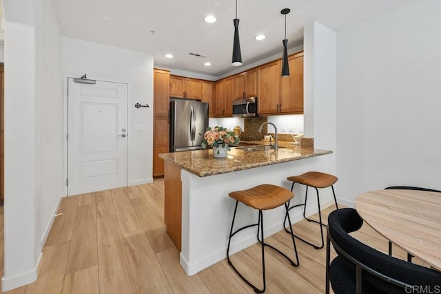 kitchen with sink, dark stone countertops, hanging light fixtures, stainless steel appliances, and kitchen peninsula