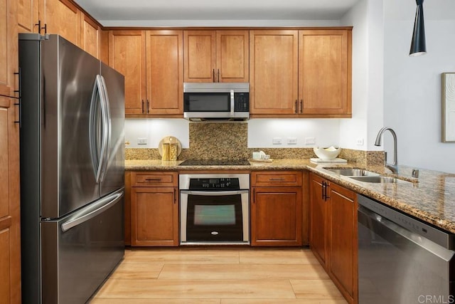 kitchen with appliances with stainless steel finishes, sink, light stone counters, and light hardwood / wood-style flooring