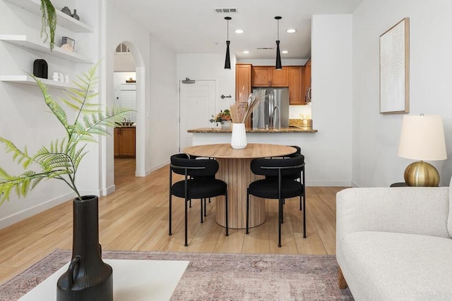 kitchen with stainless steel fridge, kitchen peninsula, hanging light fixtures, and light hardwood / wood-style flooring