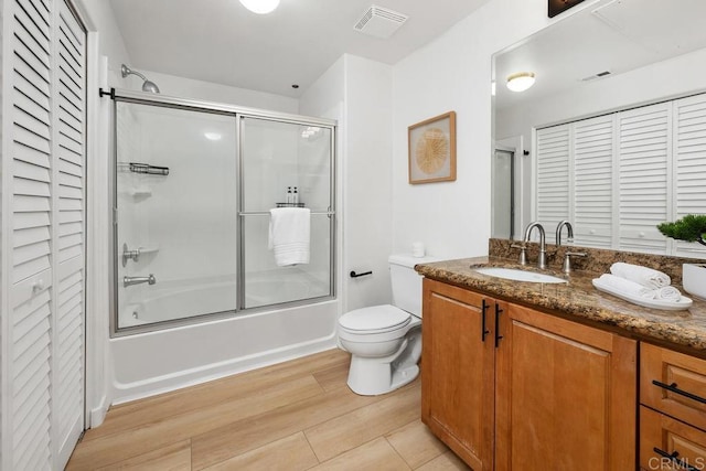 full bathroom with hardwood / wood-style flooring, bath / shower combo with glass door, vanity, and toilet