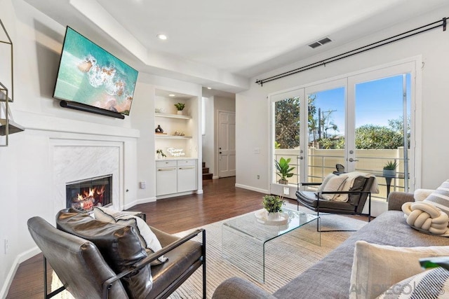 living room featuring built in shelves, a premium fireplace, and dark wood-type flooring