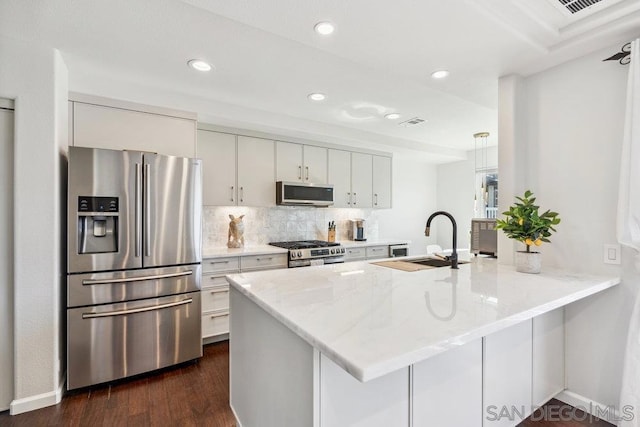 kitchen with appliances with stainless steel finishes, kitchen peninsula, sink, and white cabinets