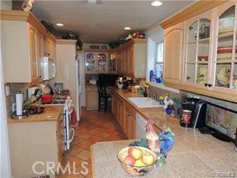 kitchen with light tile patterned flooring, sink, light brown cabinetry, and white appliances