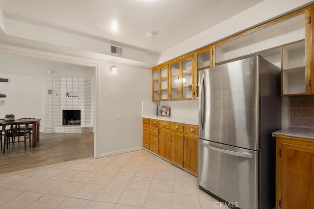 kitchen with stainless steel refrigerator, light tile patterned flooring, a brick fireplace, and backsplash