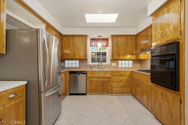 kitchen featuring a skylight, sink, decorative backsplash, exhaust hood, and stainless steel appliances