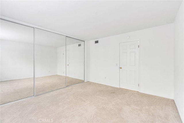 unfurnished bedroom with light colored carpet and a closet