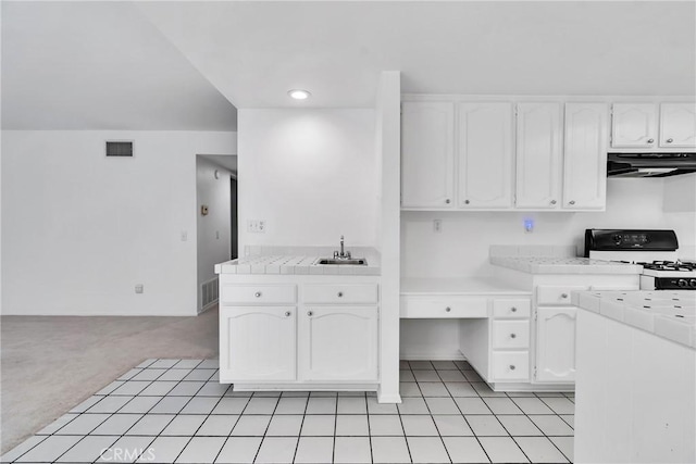 kitchen with sink, range hood, white cabinets, gas range, and tile countertops